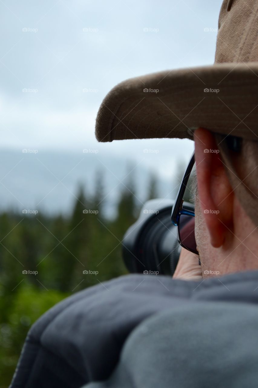 View from behind make photographer wearing hat with camera taking photograph 