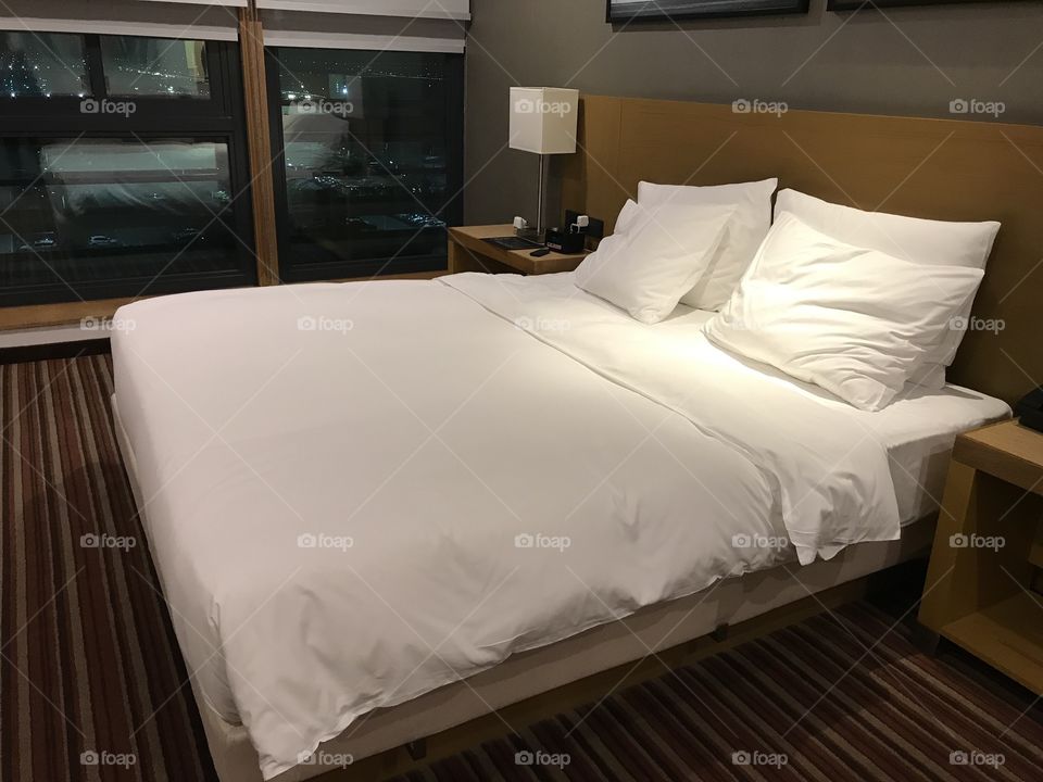 Double bed in a hotel room with white sheets and pillows with windows in the background