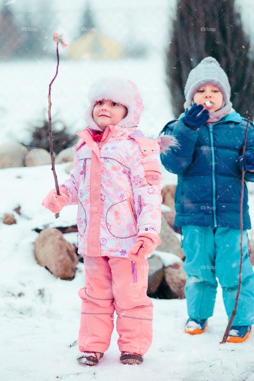 Little girl and boy enjoying marshmallows prepared over campfire outdoors in the winter. Children holding wooden sticks with toasted candies. Kids wearing warm clothes