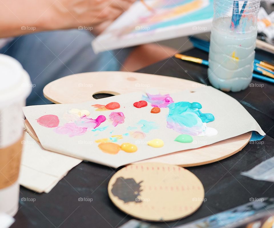 A colorful oil paint on wooden palette. Abstract blur of artist painting on the background. Selective focus on the pink acrylic color