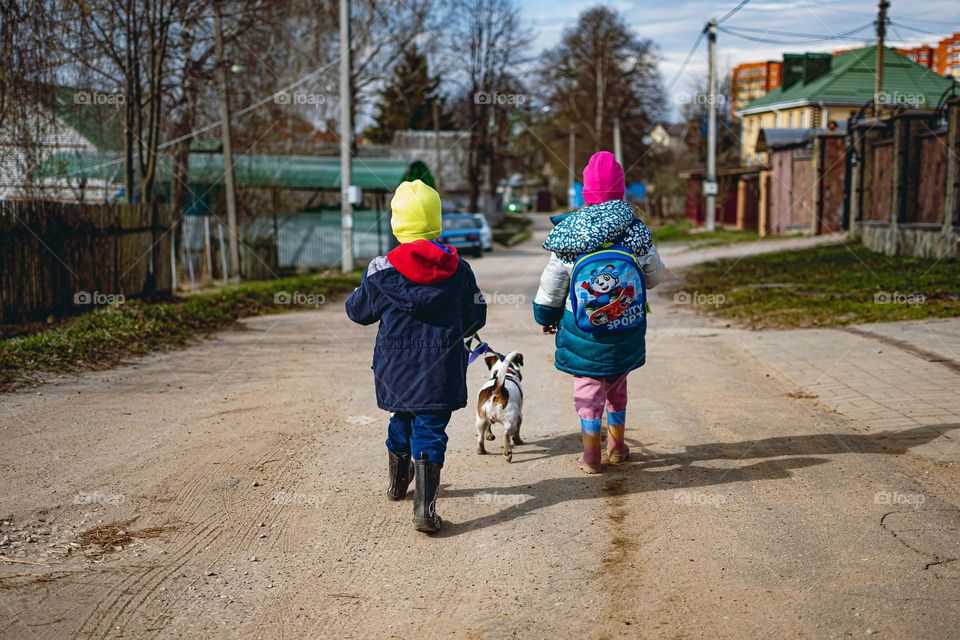 Children walk down the street with a dog on a leash.