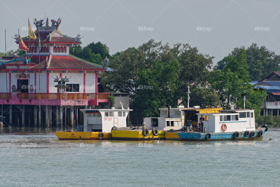Idle time at the port. Men fishing off their anchored boats with a Chinese Temple on stilts in the background. Port Klang, Malaysia. June 2018