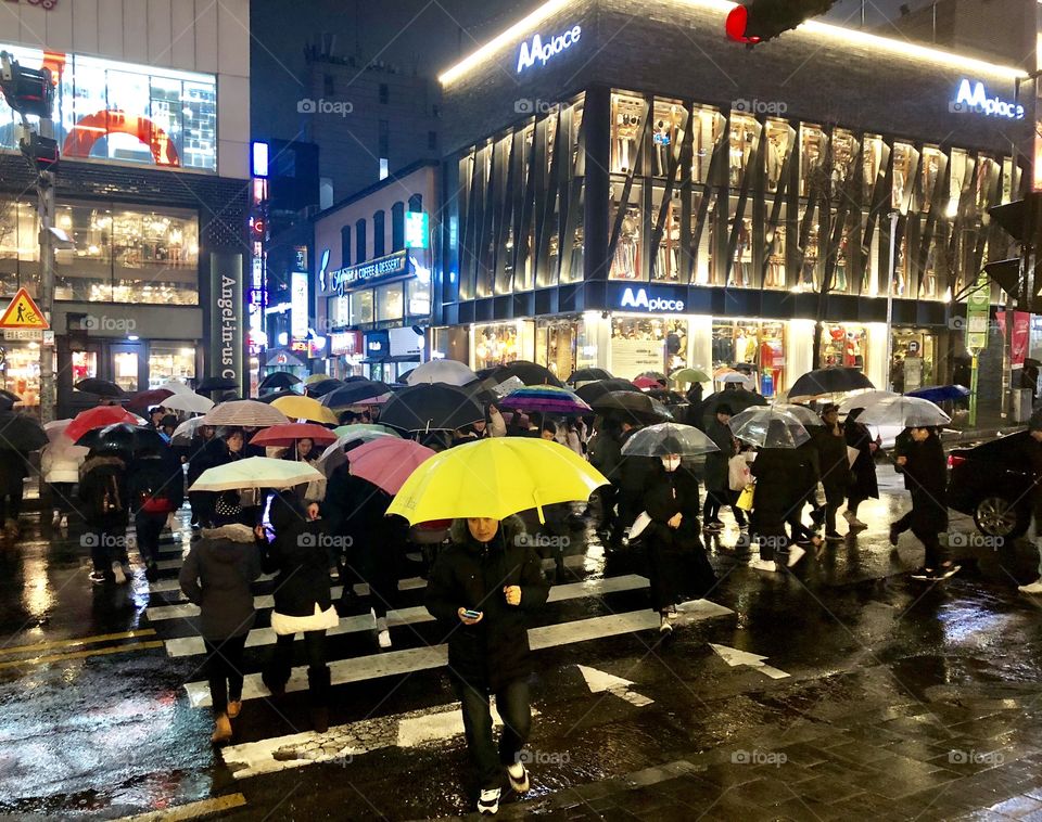 A colorful nighttime scene in a bustling city in Asia. It wasn’t a particularly heavy rain, but people did not want to feel the water. The colorful large umbrellas made for a stunning scene. 