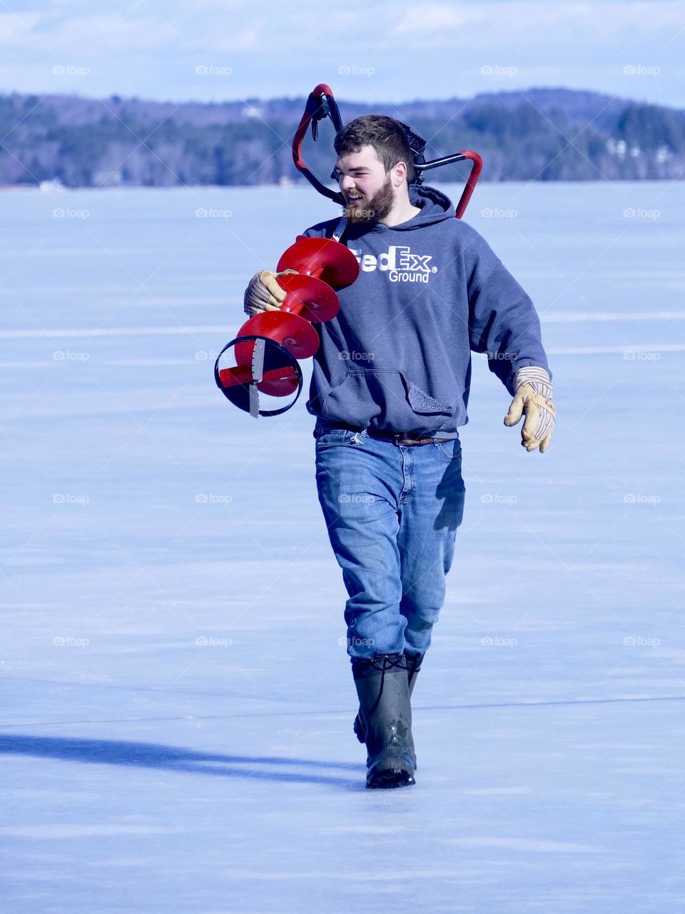 A young man carries an ice auger on his shoulder after drilling holes in the lake ice.