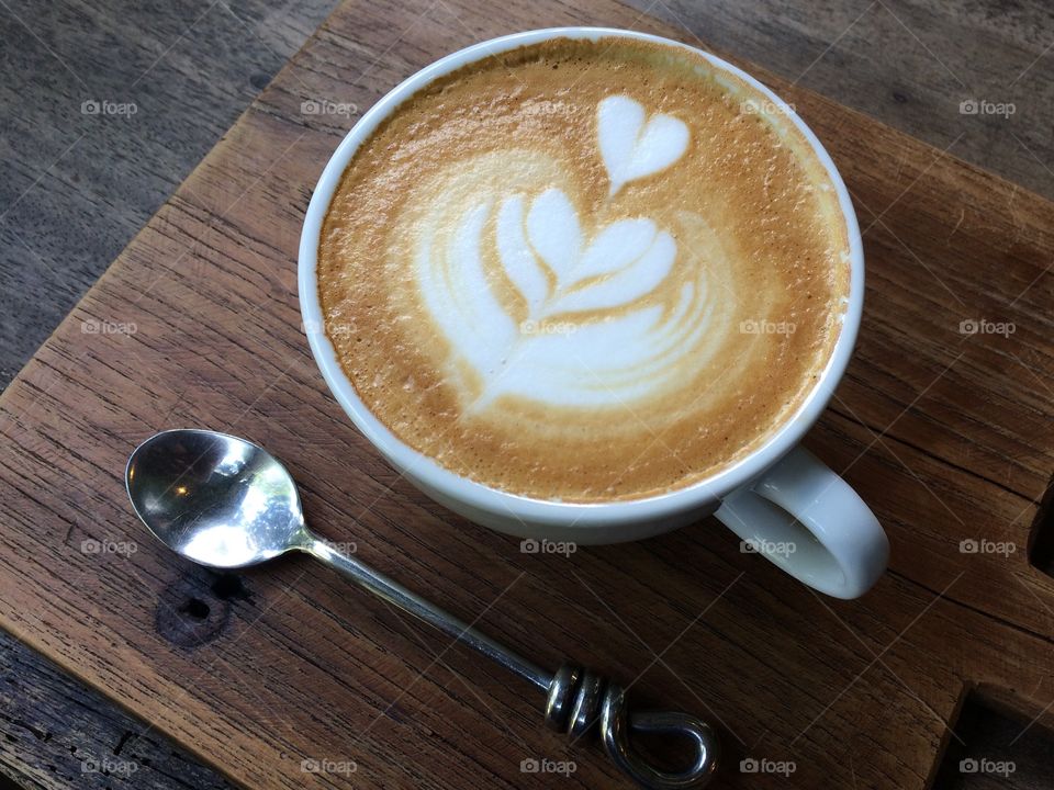 Hot latte art heart shape with stand-less steel spoon on wooden tray   