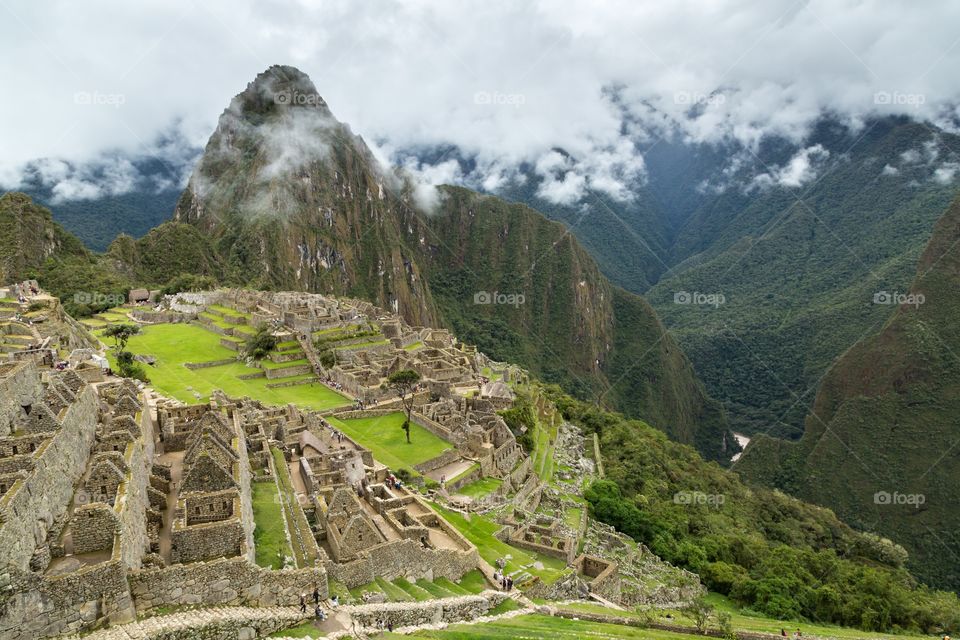 View towards Machu Picchu. View towards famous Machu Picchu. Deep valley on the right hand side. Ruins on the left hand side. Cloudy sky