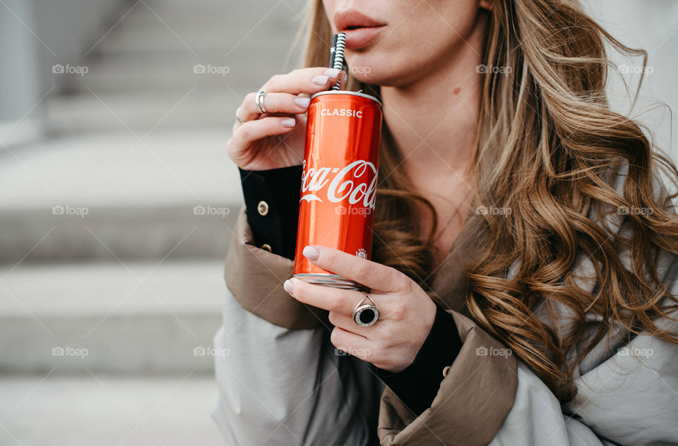 A woman holds and drinks Coca-Cola outdoors