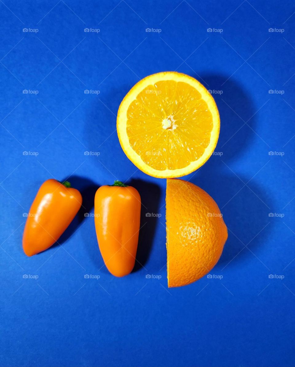 Orange and blue complementary colours flatlay made on a blue surface with two halves of a fresh orange and orange little peppers