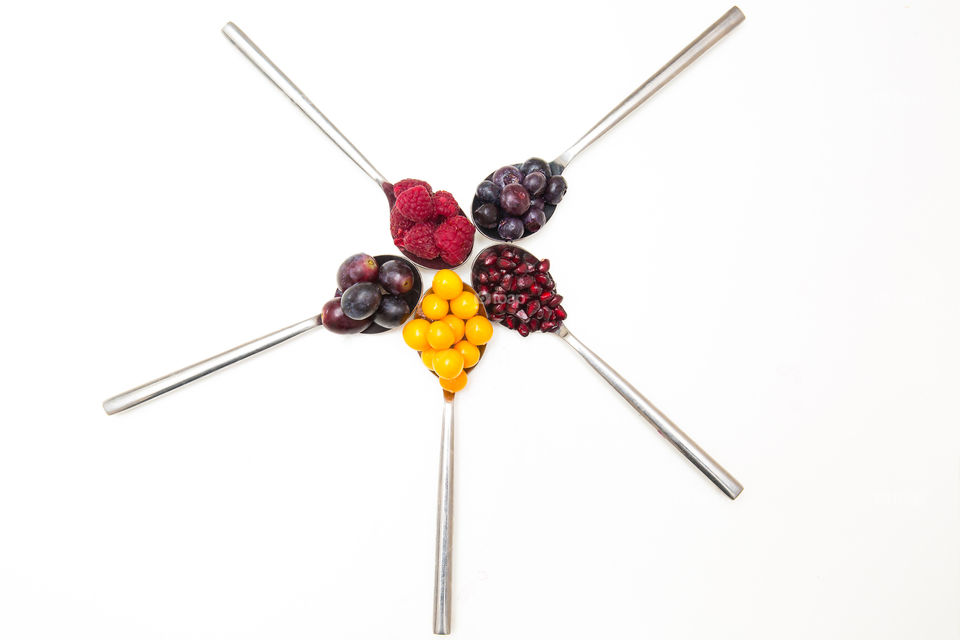 Variety of fresh delicious summer fruits arranged on a white background. Fresh grapes blueberries gooseberries raspberries and pomegranates. Flat lay image.