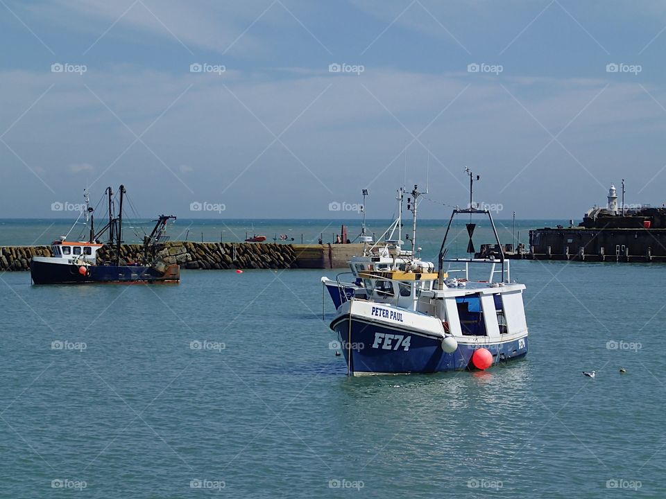 A bright blue fishing boat anchored in the harbor in Folkestone, England on a sunny summer day. 