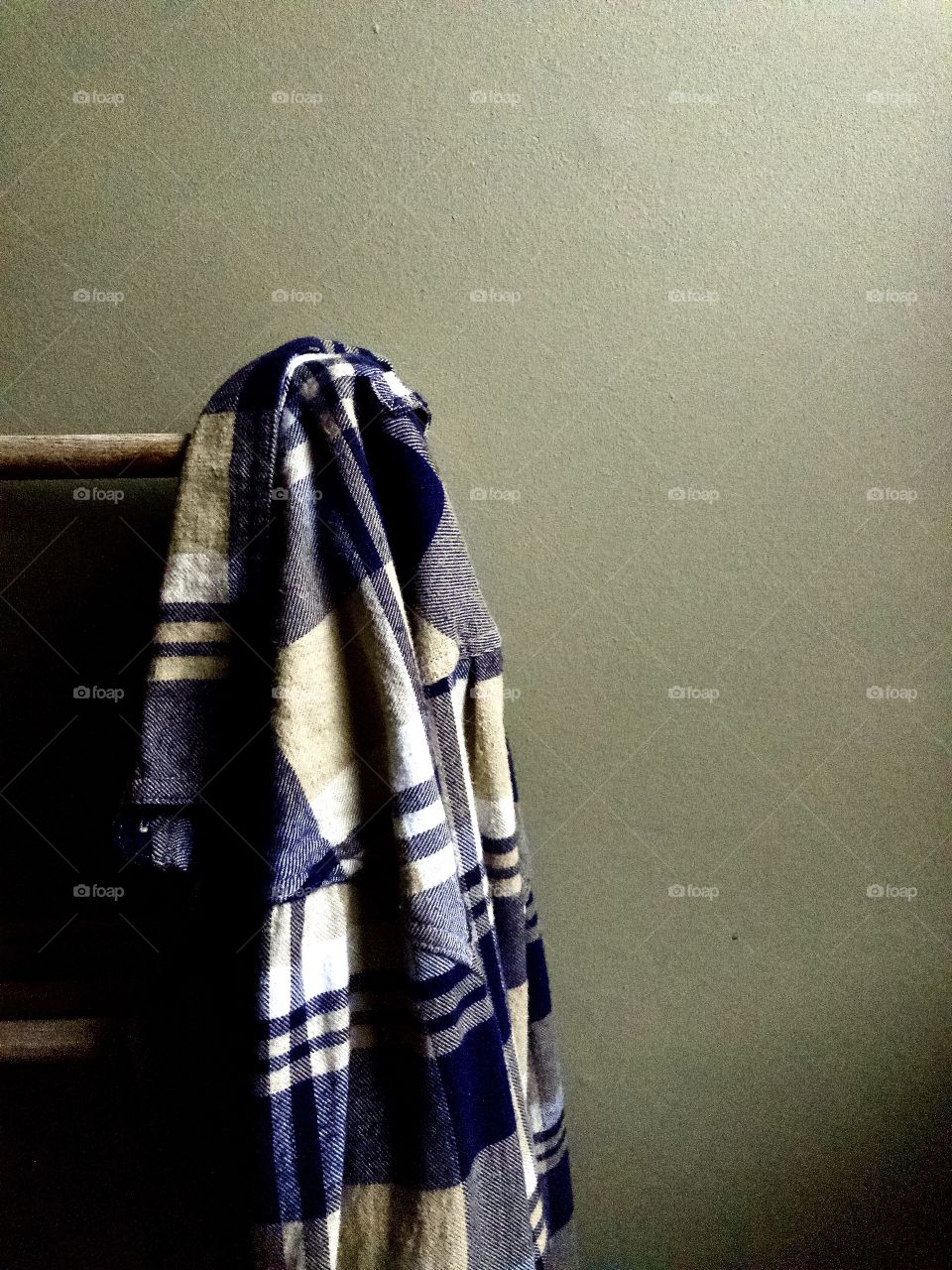 Blu plaid flannel shirt hanging on wooden clothes rack 