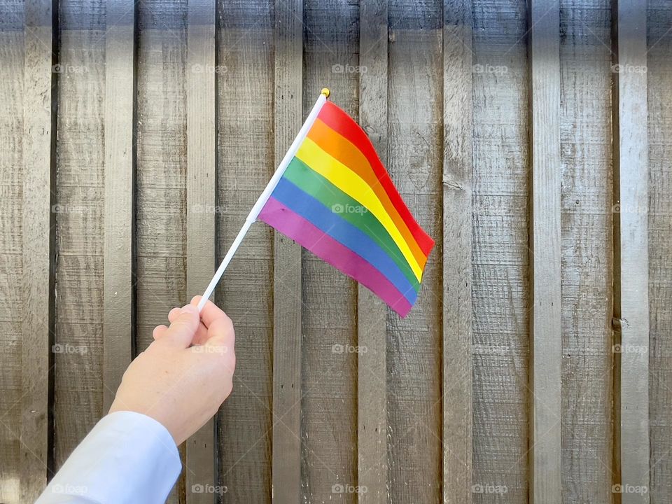 Male hand holds pride flag on the wooden background 