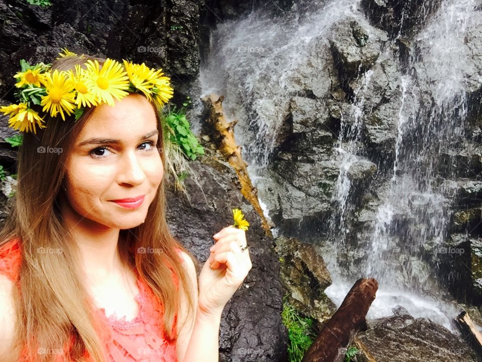 Portrait of woman with flower crown made of yellow flowers and waterfall in the background 