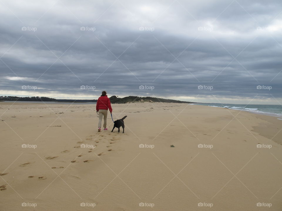 Empty beach walk and play , woman with black Labrador