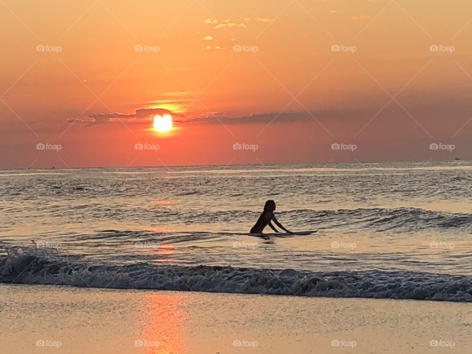 Surfer glides into the ocean under the morning sunrise