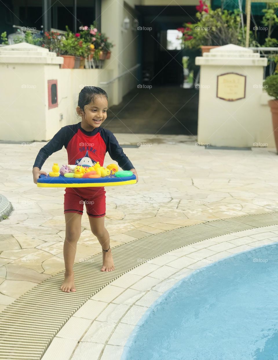 A 4 year old girl playing with floating ducks and rings at swimming pool and she has a beautiful smile on her face at summertime 