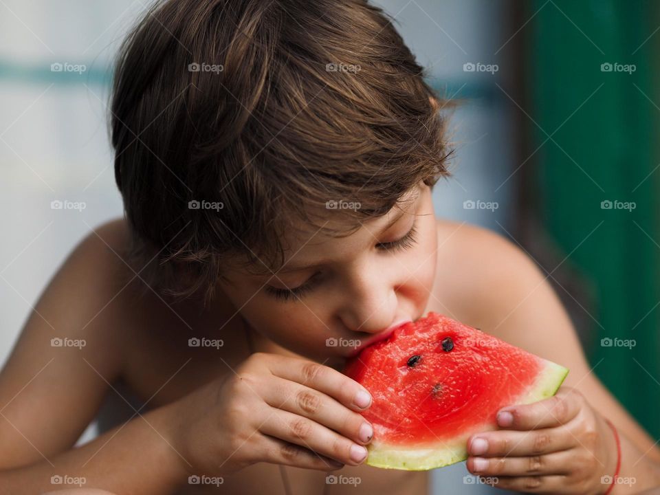 Cute little boy eating fresh watermelon on a street in summer day, portrait of child 