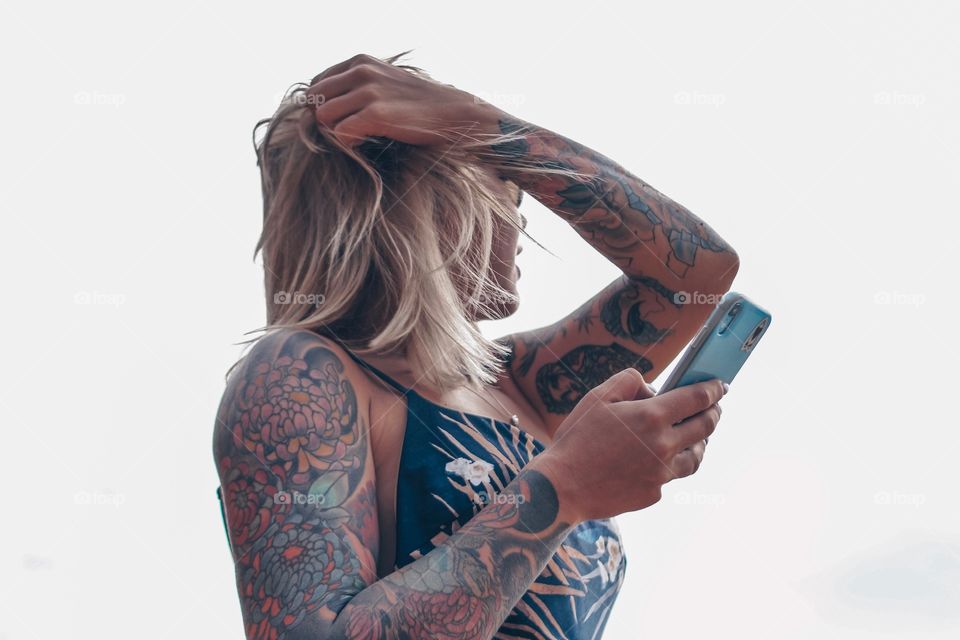Young lady with tattoo hands sent a message on her smartphone 