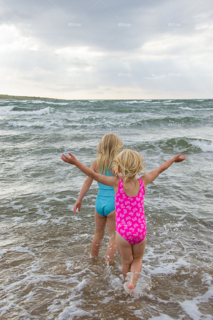 Twi sisters playing at the beach of Tylösand outside Halmstad in Sweden. It's about to get stormy weather but the girls is having fun swimming and playing in the water.