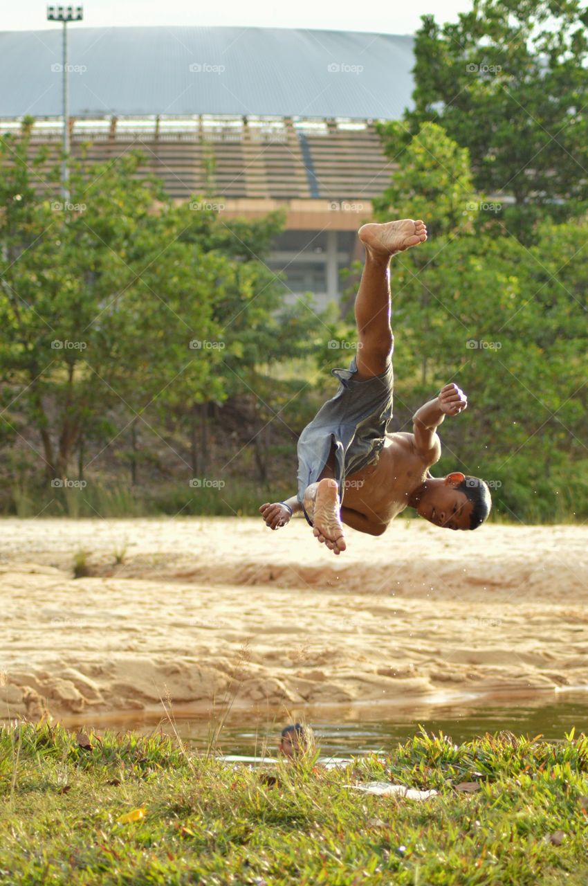 this child is jumping from the edge of the river, he loves doing that with acrobatic movement
