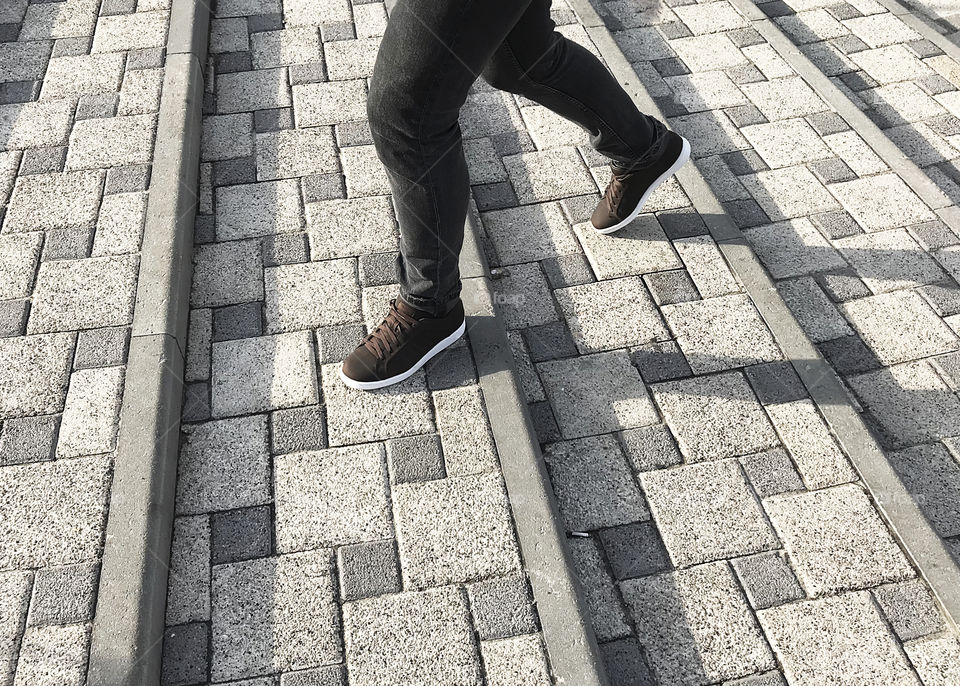 Male feet walking by the street steps with a pavement made of grey squares pattern 