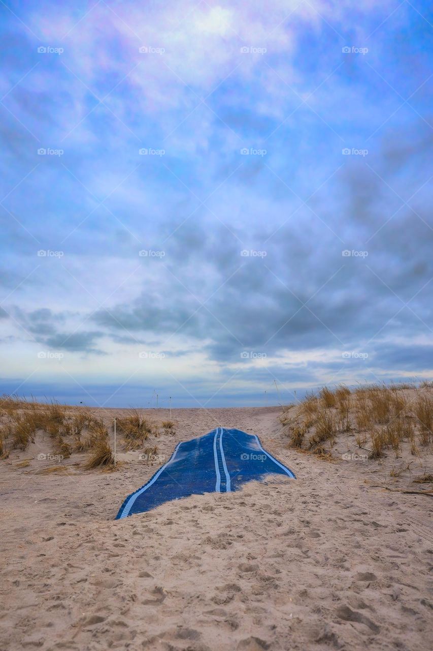 Beach pathway partially covered by wind swept sand, under a soft pastel colored sky