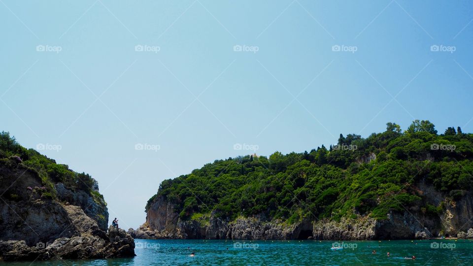 Paleokastritsa beach view with person perched on rock, Corfu, Greece