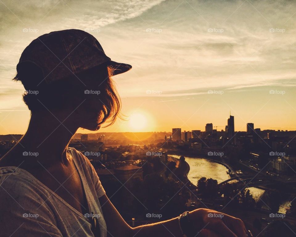 Silhouette of a girl enjoying sunset above the city of Vilnius.