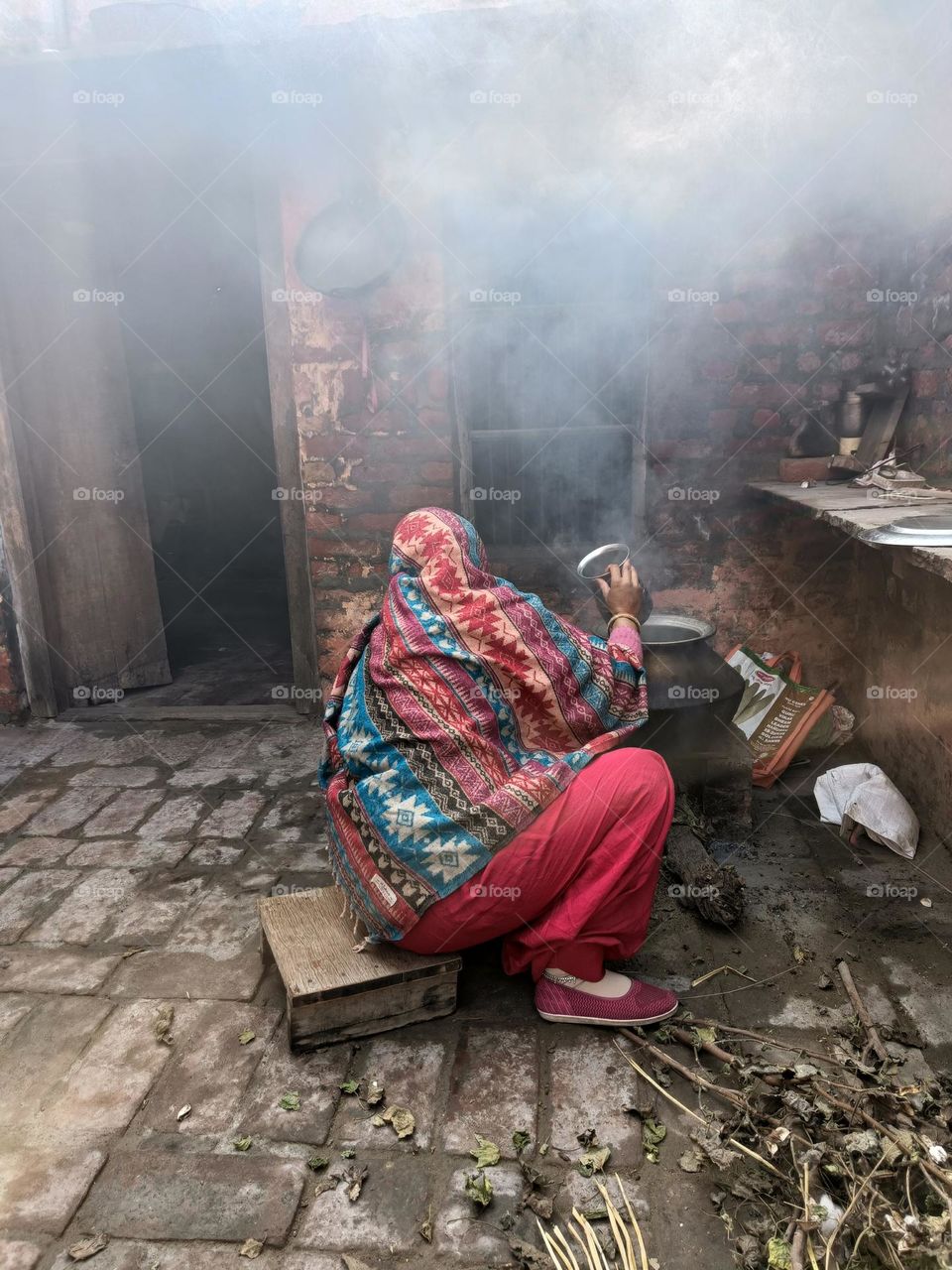 a lady using wood burning to get hot water in winters.