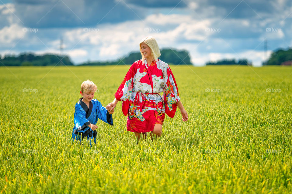 Blonde woman and boy, dressed in kimono, go through the field of crops