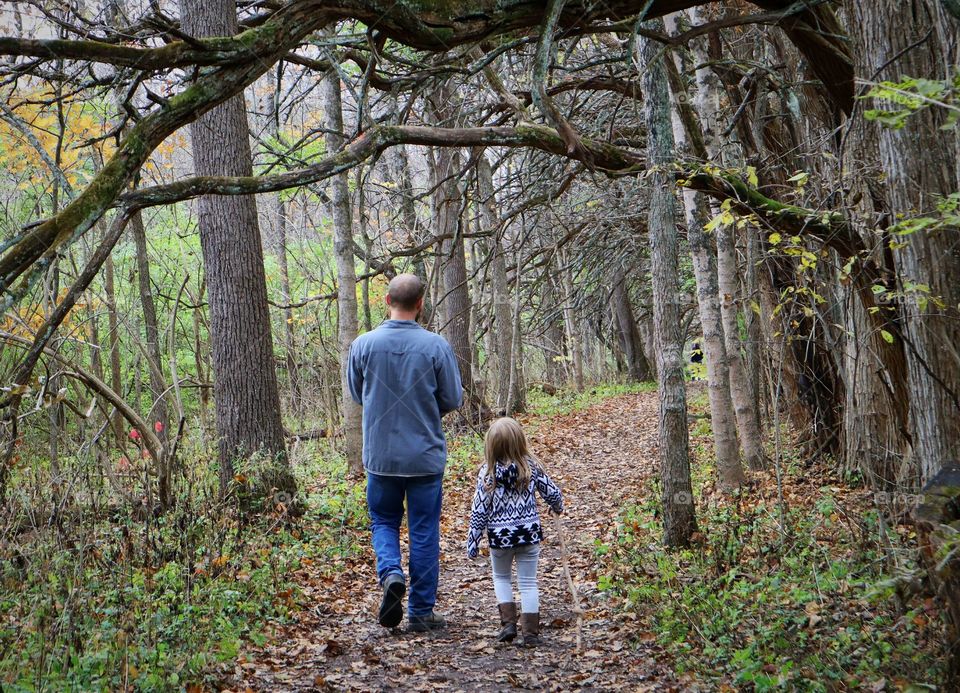 father and daughter walking thru the woods in autumn