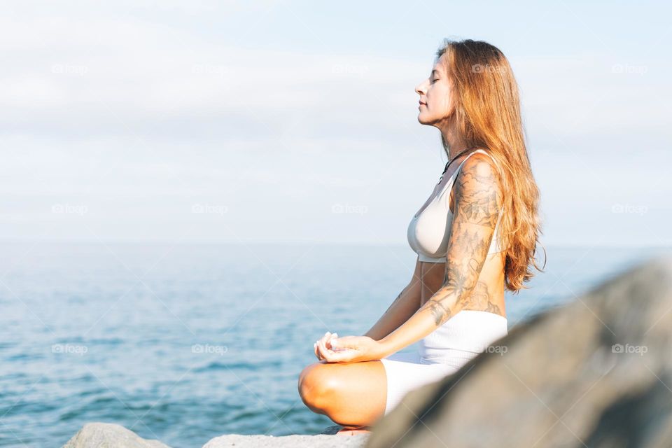 Crop photo of young fit beautiful woman with long hair in white sport clothes practice yoga and enjoy life on the sea beach, mental and phisical health