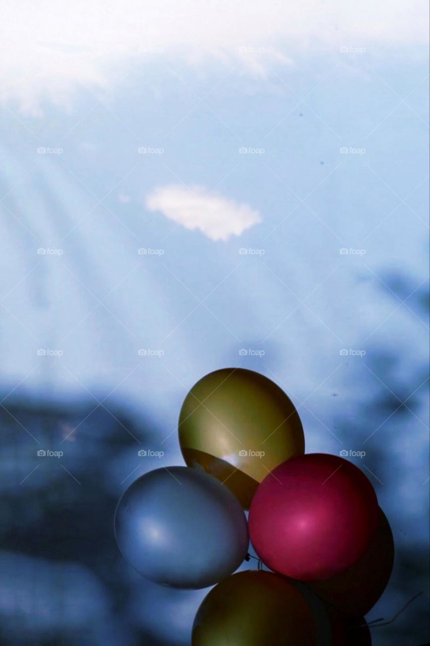 Looking through a window at three colorful balloons and blue sky with clouds