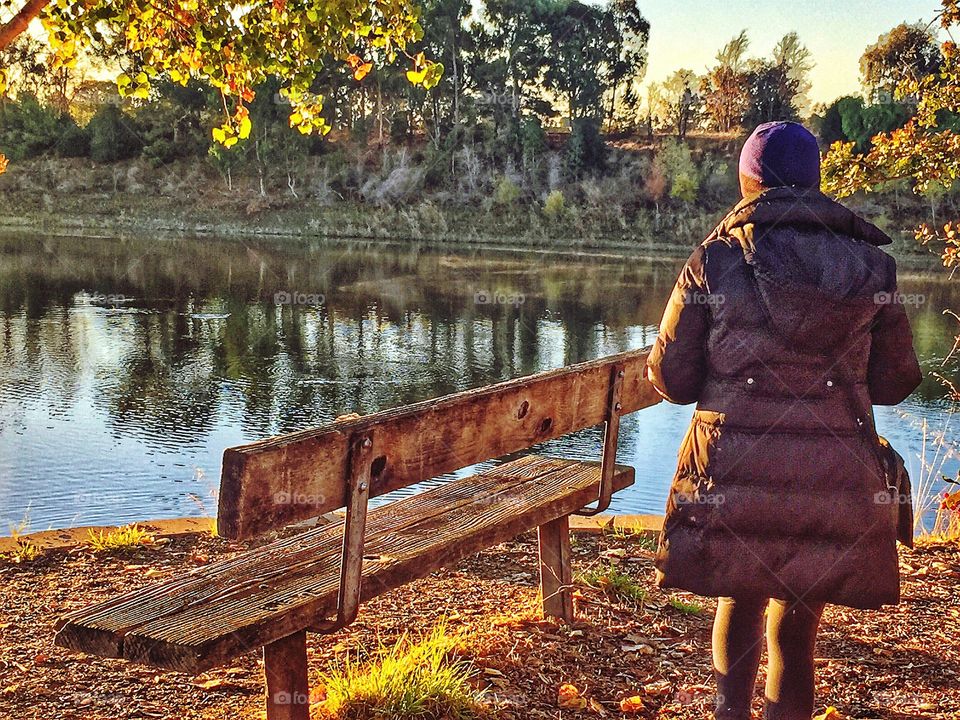 A lady from behind wearing her warm, puffy winter jacket while taking in the Autumn view of the beautiful lake.