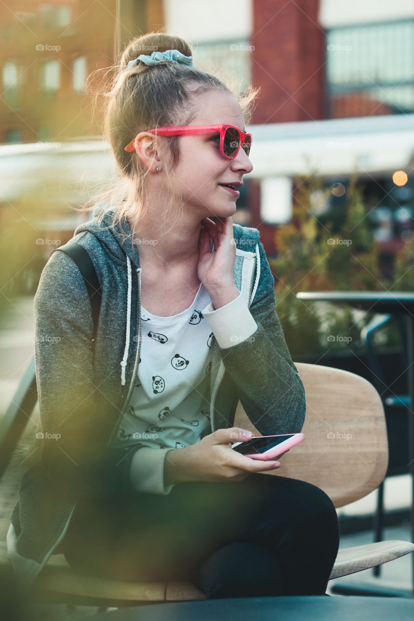 Teenage girl having fun using smartphone sitting in center of town