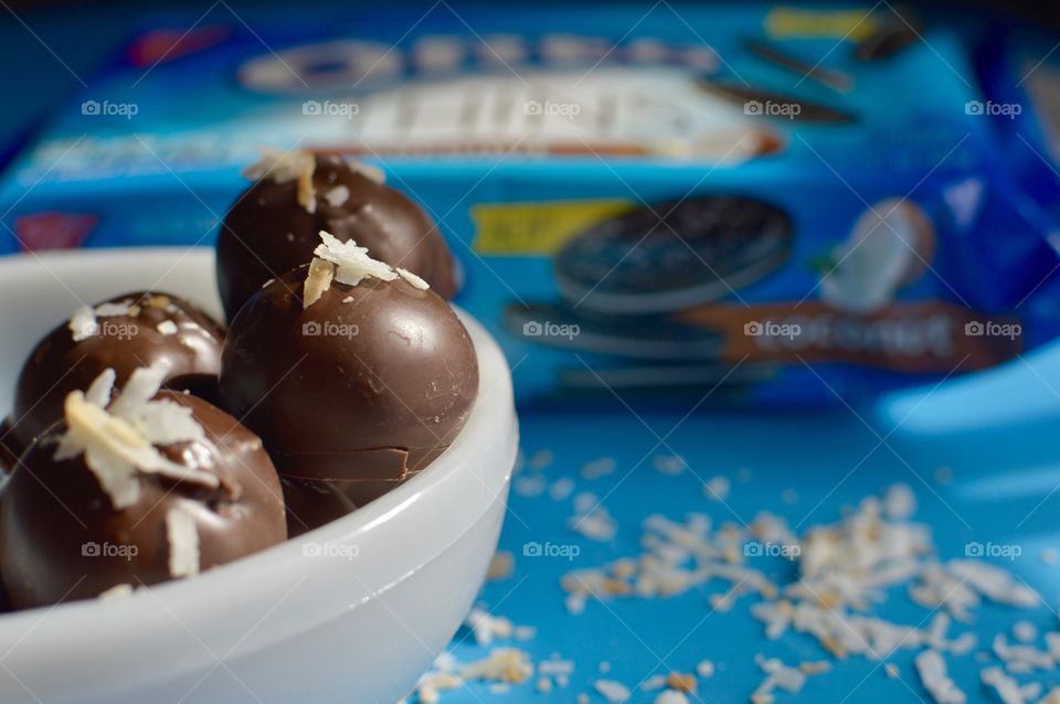 coconut Oreo thin cookies on a blue background with coconut shreds with truffles in a white bowl 