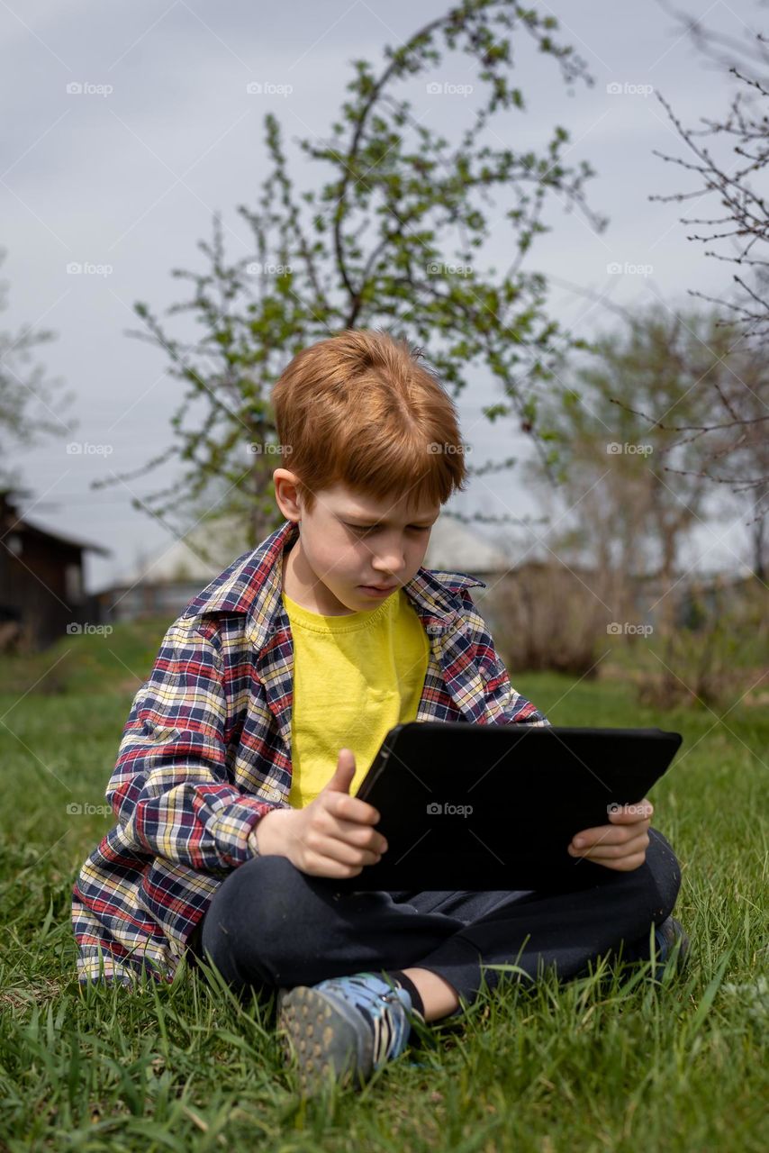 Red-haired boy watching a movie on a tablet with a garden
