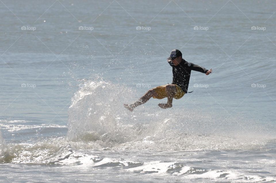 Surfer falling off board, in the air above the water