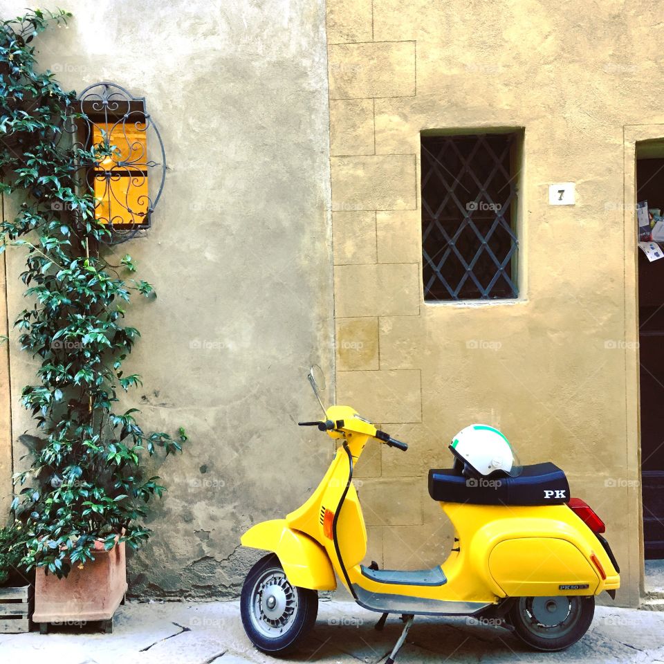 A yellow Vespa stopped outside a store in Pienza, Italy