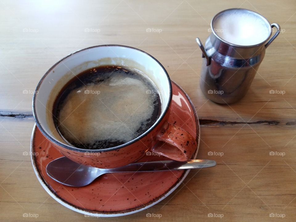 black coffee served on wooden table in red orange cup with milk in cute mini milk can