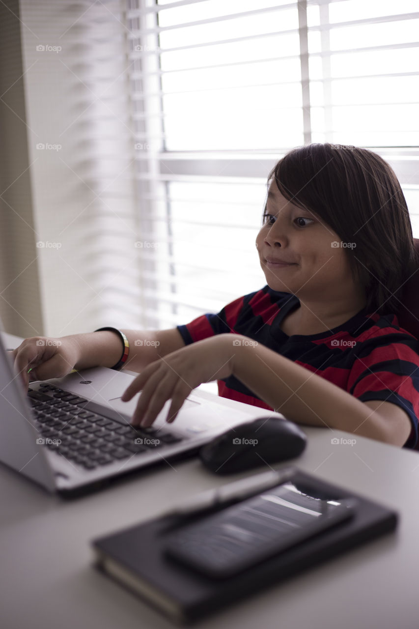 young Eurasian boy making funny facial expression working on a laptop at the office