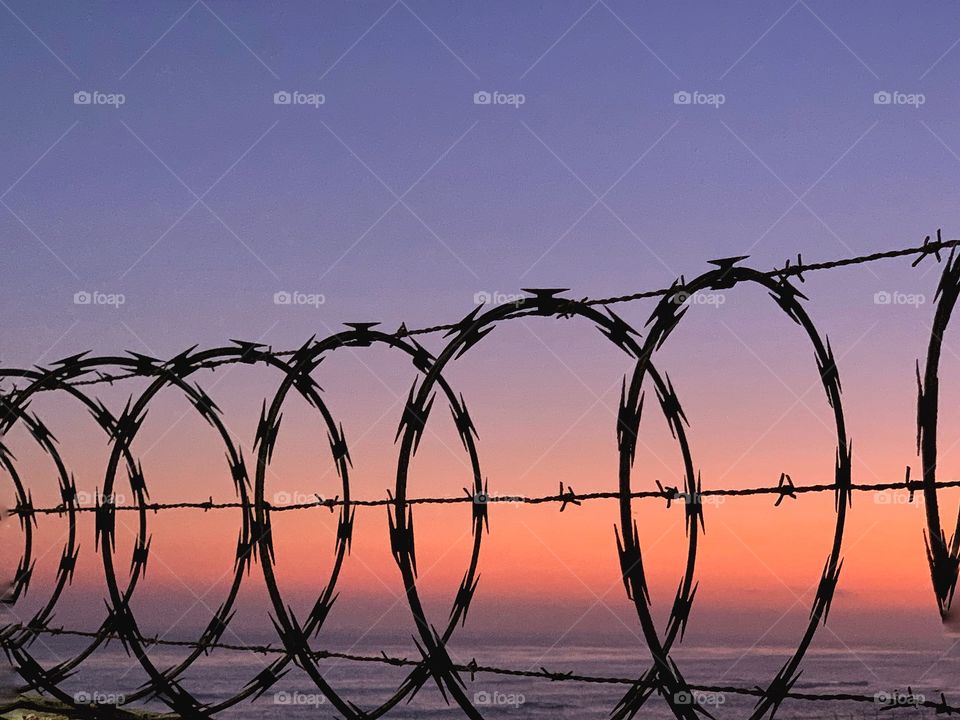 Razor wire at sunset overlooking Pacific Ocean