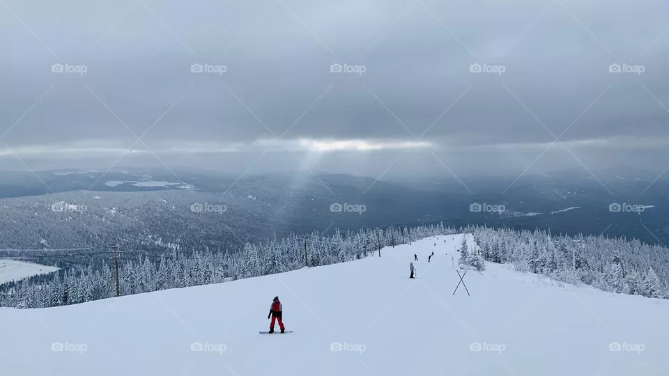 The outgoing ray of the sun shines through the clouds on the ski slope
