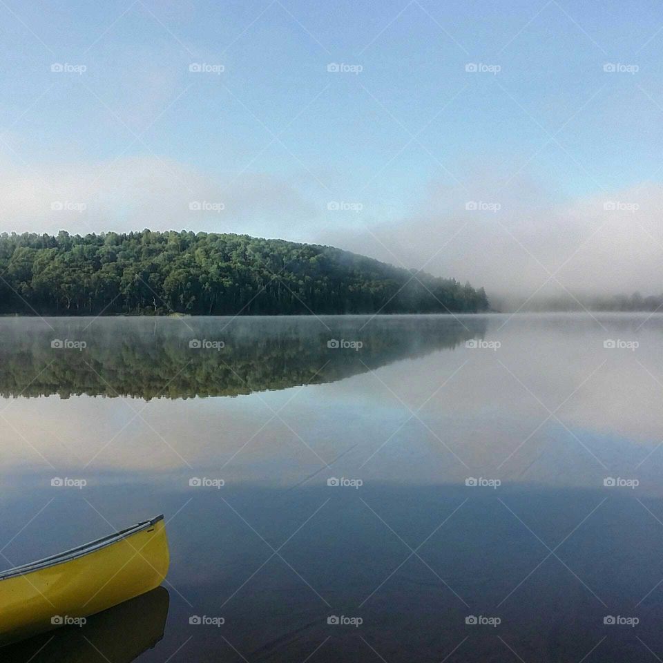 Mountains reflected on a lake on a foggy morning and a  yellow canoe
