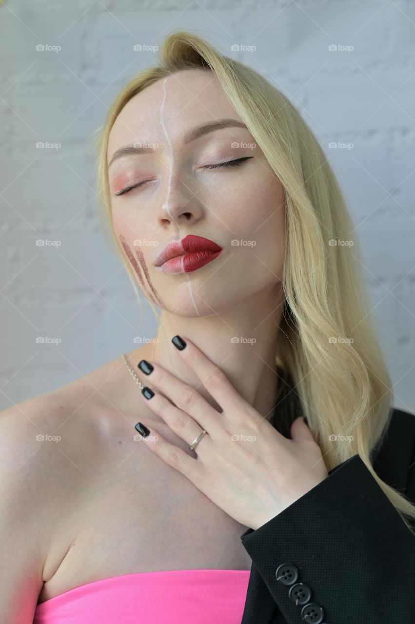 Close-up portrait of a blonde girl with different make-up on half of her face and with hand on the neck on white background