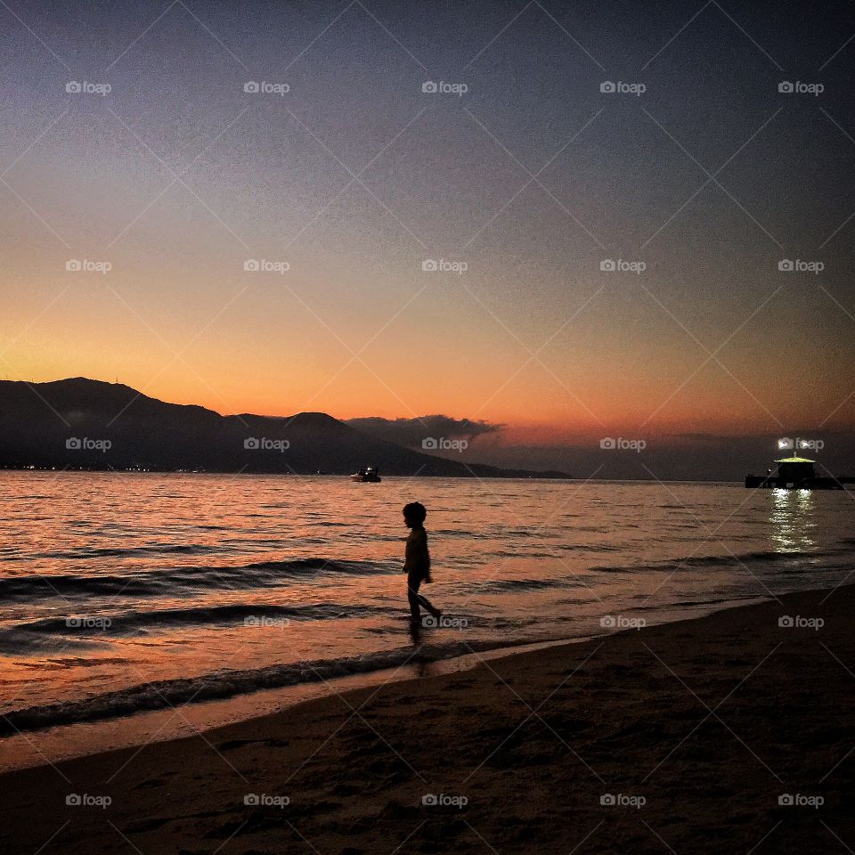 The lonely boy . A little boy walks alone to the sea in a beautiful sunset in Ilhabela. 