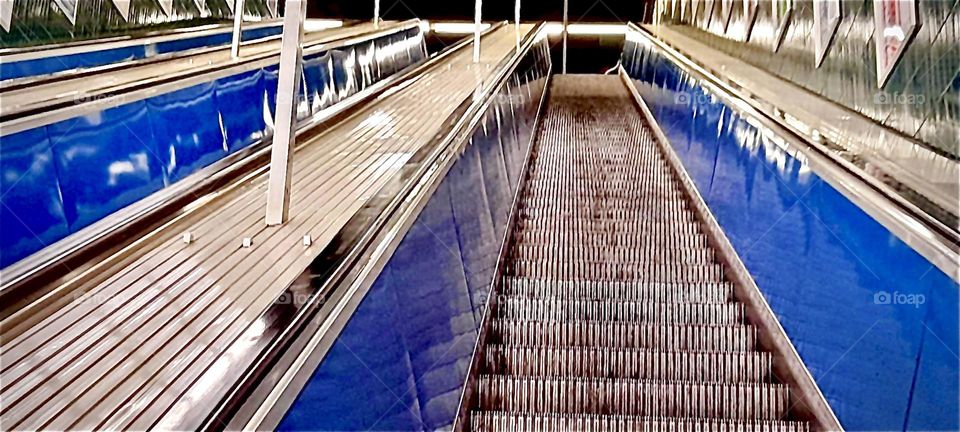 This is an escalator leading through the various underground tunnels and walkways that go from the various streets on ground level to the stations of the “Munich” subway. 2022. Hypnotic Productions