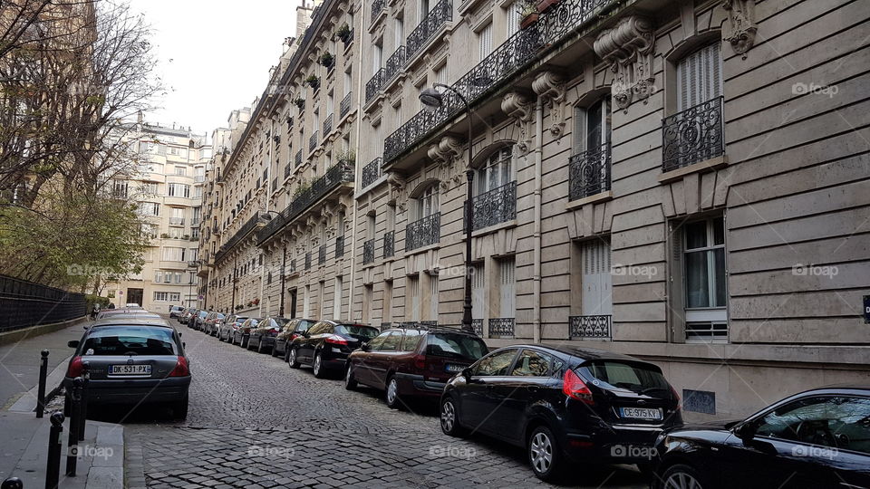 A picturesque small cobblestone street in Paris lined with cars on each side of the road.