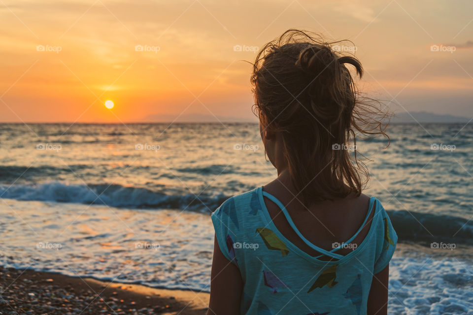 Girl admiring sunset on pebble beach.