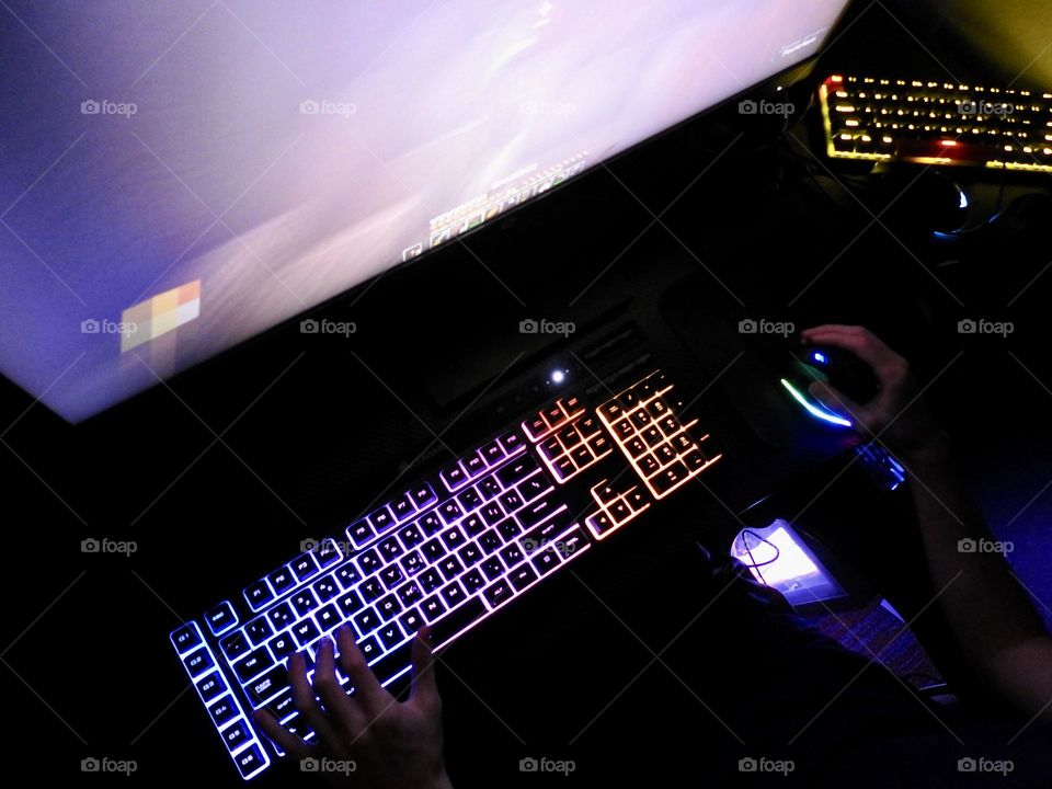 Teenager boy playing Minecraft on the gaming computer seen from a high angle and seeing his hand playing using the keyboard and the mouse accessories in a dark room.